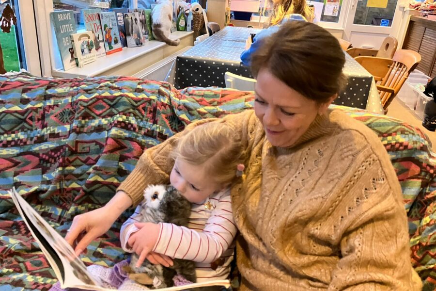 A women sat on a sofa with her arm around a small girl reading a book together