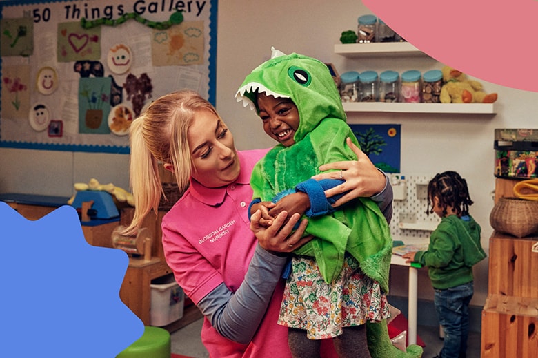 A woman holds a child dressed as a dinosaur in a classroom.