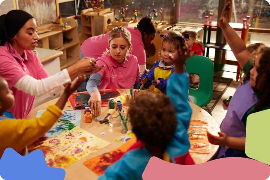 A group of children sitting with two women around a table in a playroom.