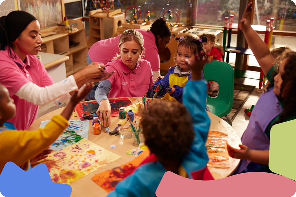 A group of children sitting with two women around a table in a playroom.