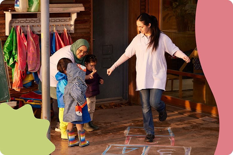 Two women play playing hopscotch with a group of children.